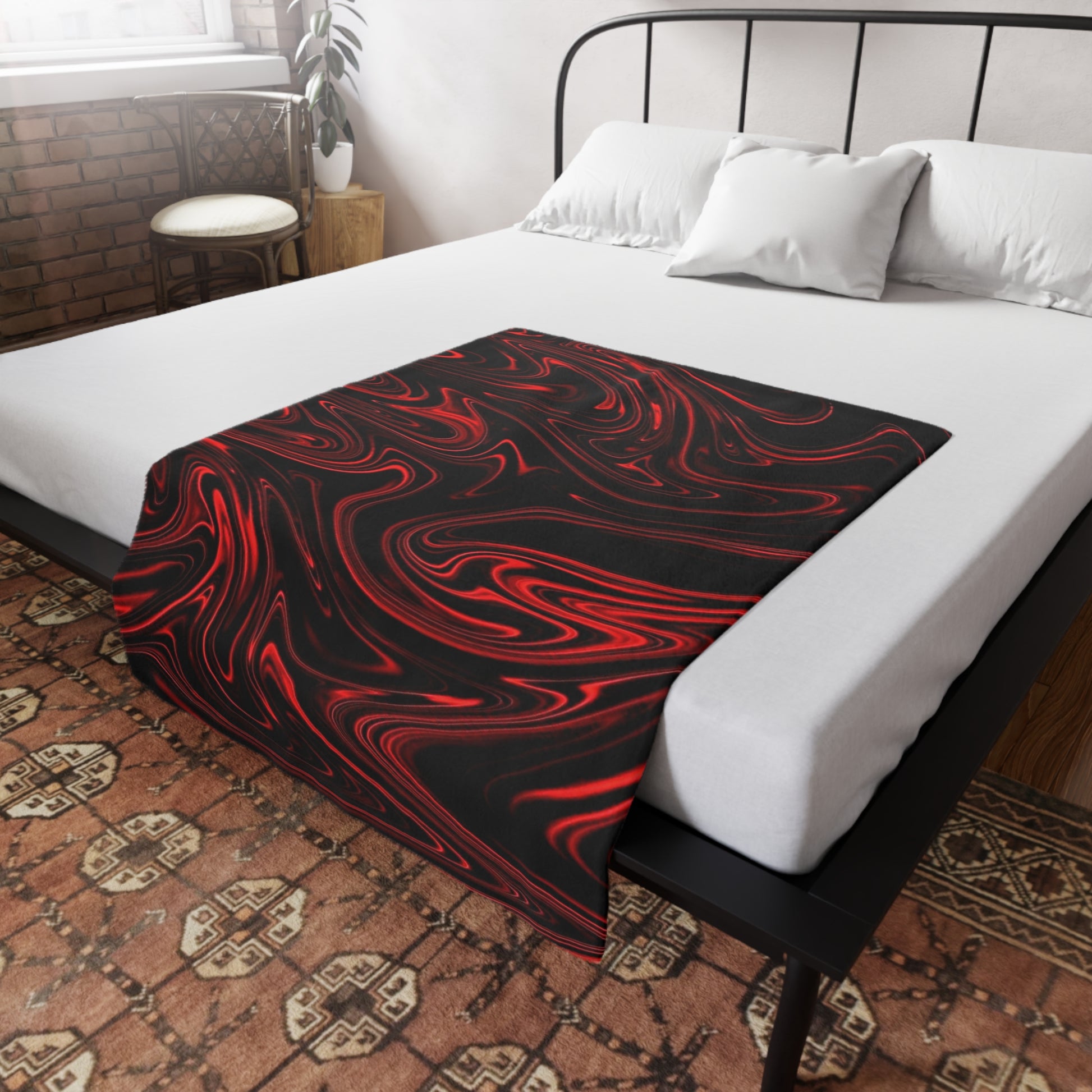 A black and red swirl-patterned blanket spread flat across a white bed in a rustic room with exposed brick and a patterned rug.