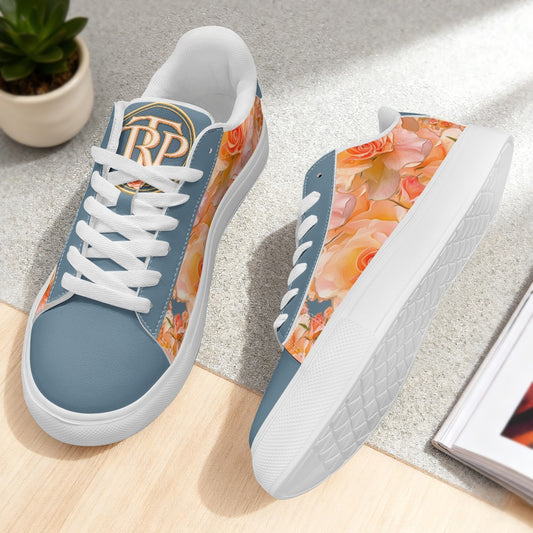 A pair of low-top sneakers shown on a light wood floor and gray surface. The shoes have a dusty blue base with a peach and orange floral print on the sides and tongue, white laces, and white soles.
