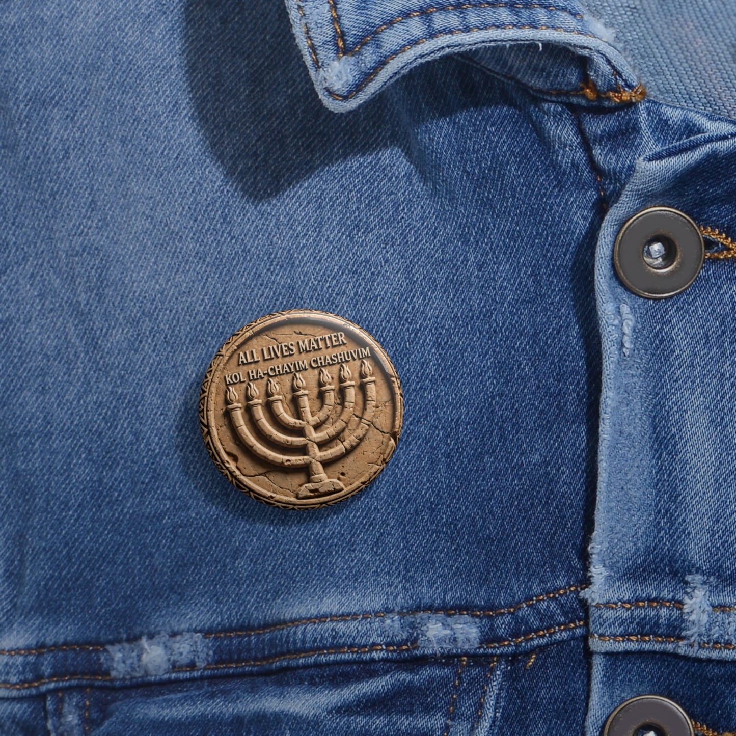 Small round stone-carved menorah pinback button featuring Hebrew and English text fastened to a blue denim jacket lapel.