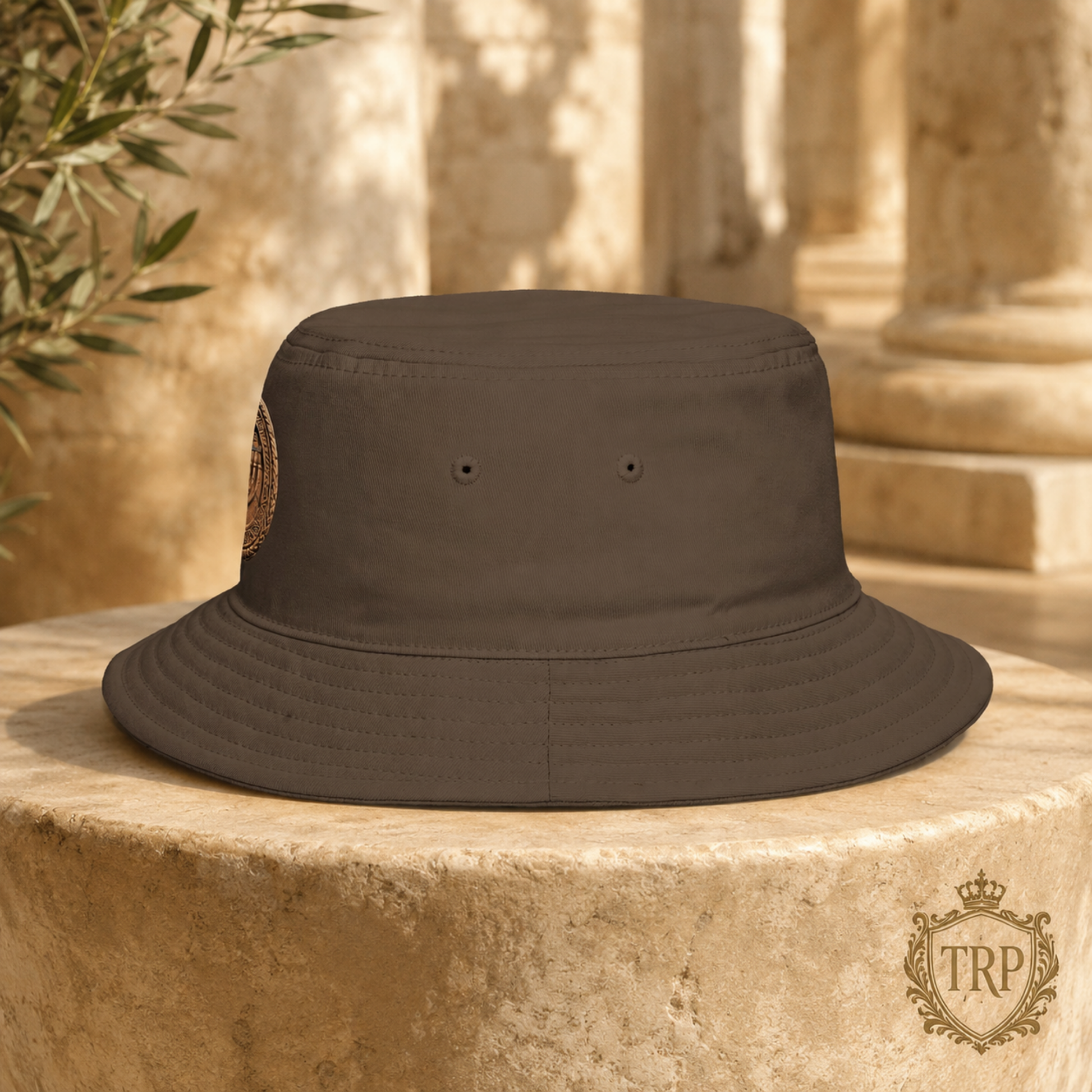 Left-side view of the brown All Lives Matter bucket hat resting on a sunlit stone pillar outdoors.
