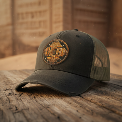 black distressed Ollie trucker cap featuring a round Hebrew World patch, resting on a rustic wooden table with a blurred desert stone backdrop.