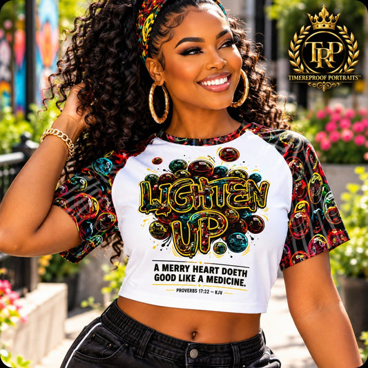 Model wearing the Lighten Up raglan crop top featuring colorful smiley bubbles and Proverbs 17:22 graphic text.