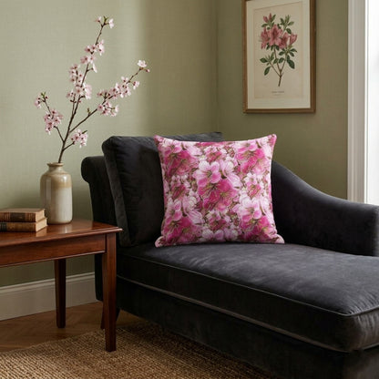 A pink cherry blossom patterned pillow rests on a dark gray velvet chaise lounge in a room with sage green walls and botanical artwork.