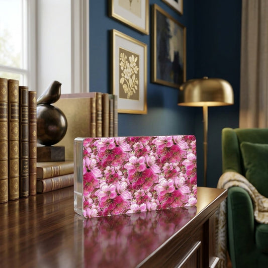 Modern acrylic block featuring a vibrant pink floral pattern, displayed on a wooden table in a sophisticated library setting with books and a green armchair.