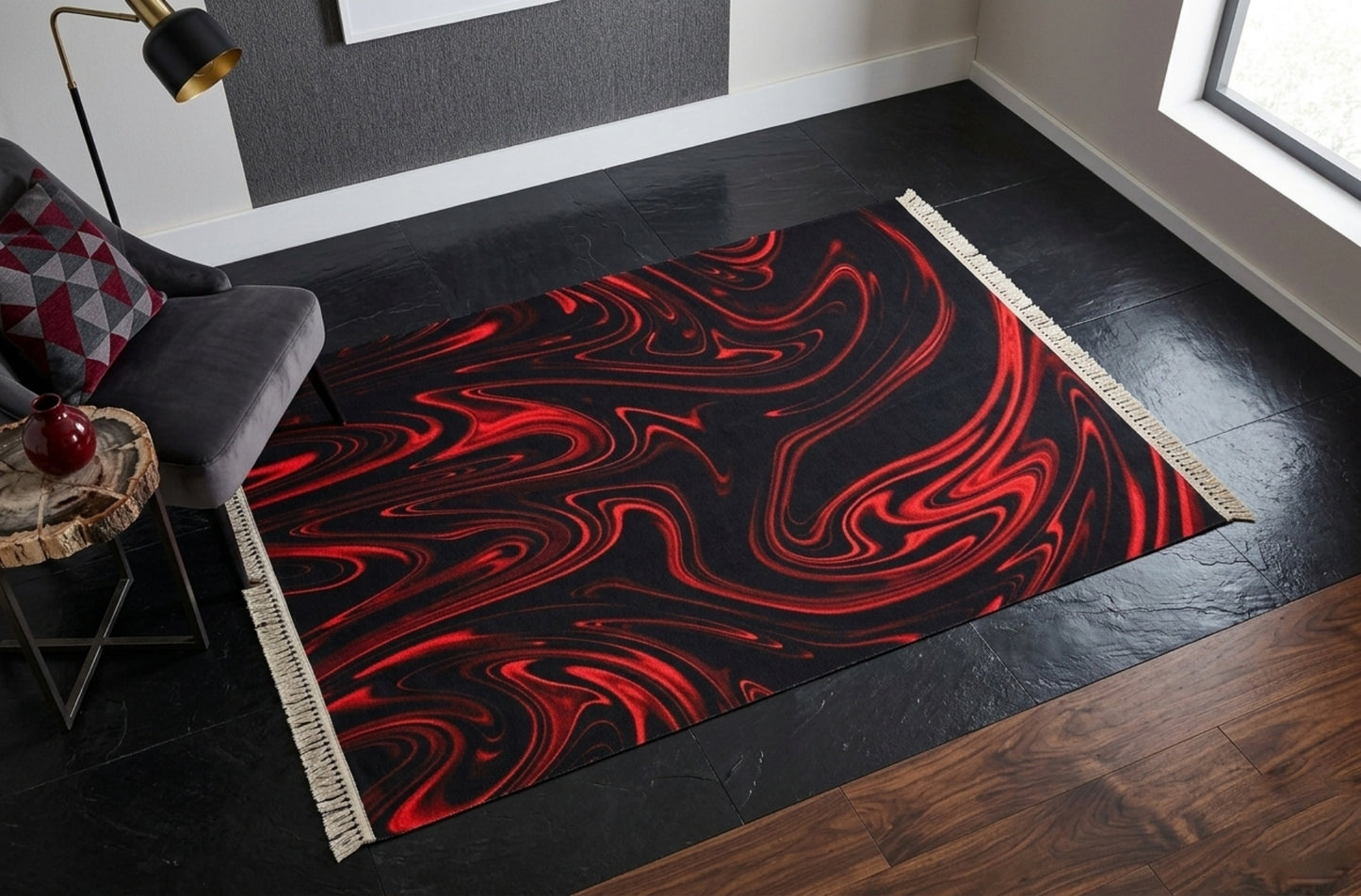 A black and red marbled area rug with white fringe in a modern room with a grey velvet chair, gold floor lamp, and black stone flooring.