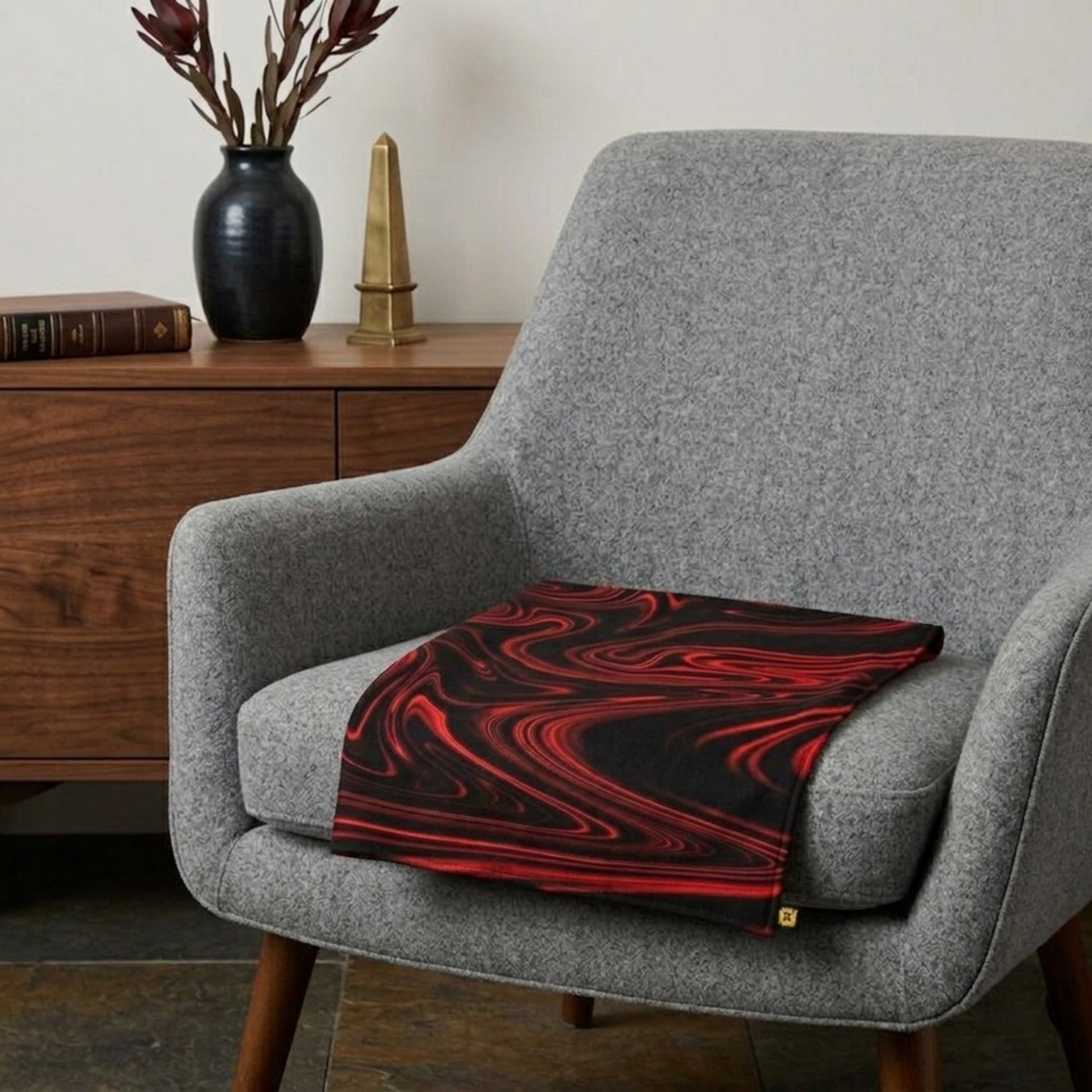 A grey textured armchair featuring a black and red liquid swirl pattern seat cushion, set against a minimalist backdrop with a wooden credenza.