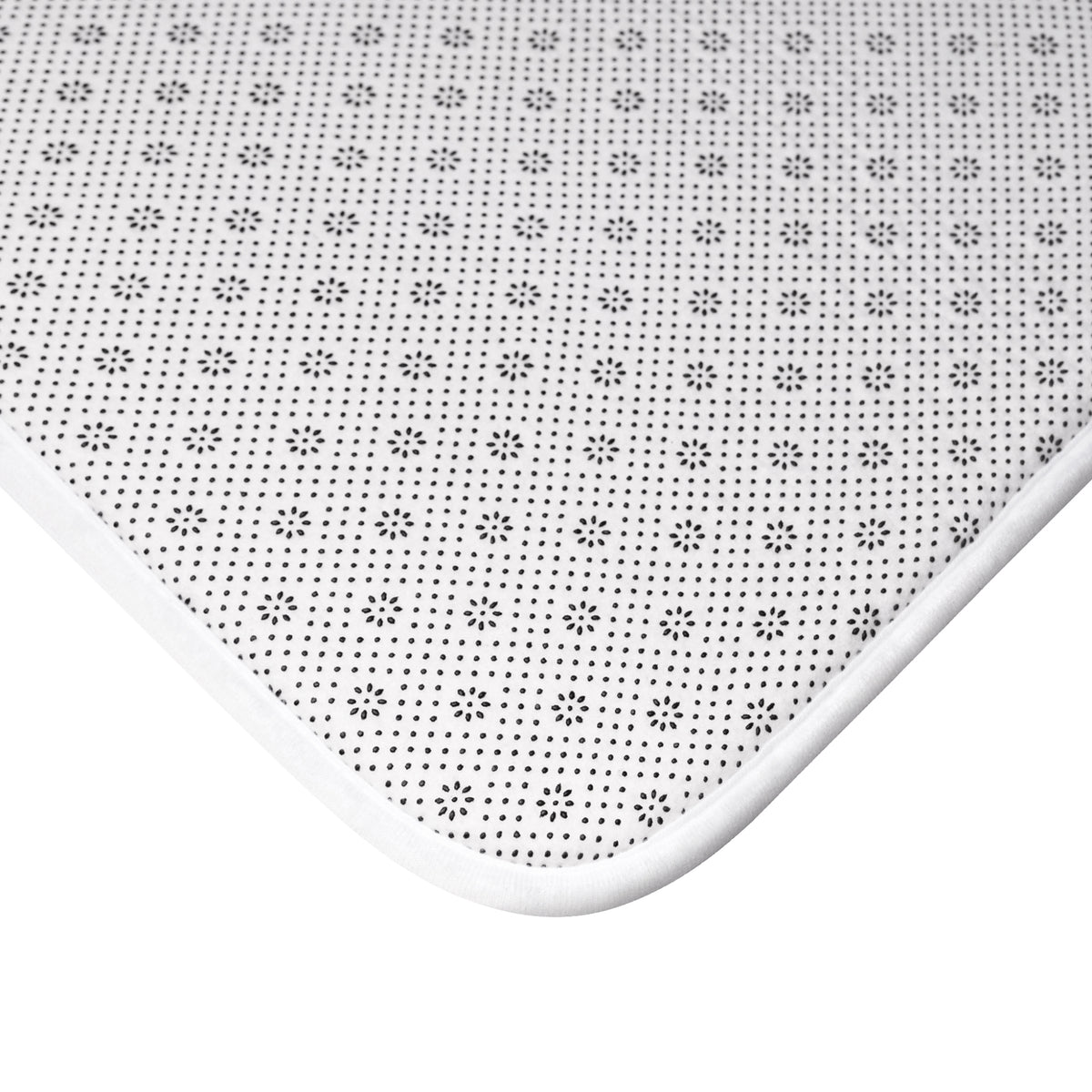 Close-up of the non-slip dotted backing, white piped border, and rounded corner of The Dawning Field bath mat.