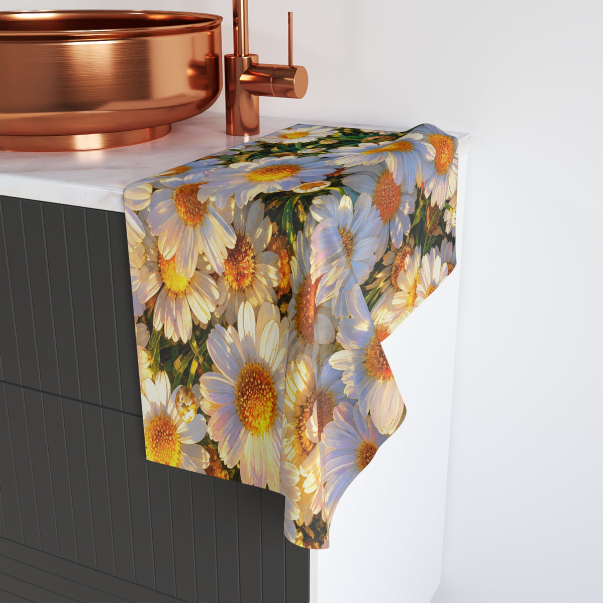 The Dawning Field hand towel draped over a dark bathroom vanity beside a round copper vessel sink, featuring white daisies in golden morning light.