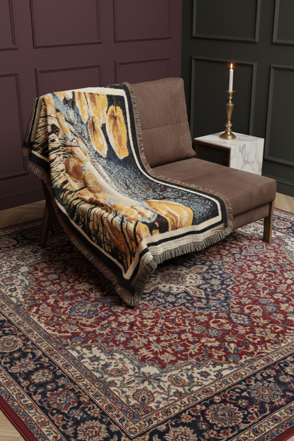 The Garden Beyond the Winter woven art throw blanket styled over a modern brown lounge chair above an ornate vintage area rug.