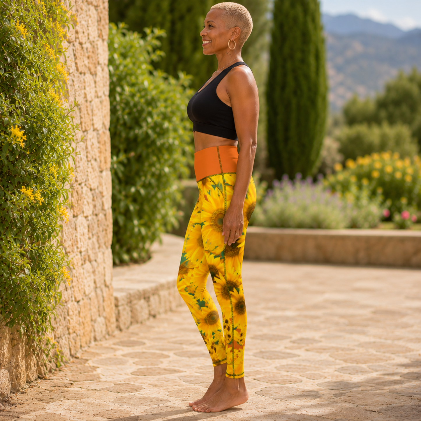 Left-side view of a barefoot woman standing by a stone wall in high-rise sunflower pocket leggings with a vivid red tangelo orange-colored waistband.